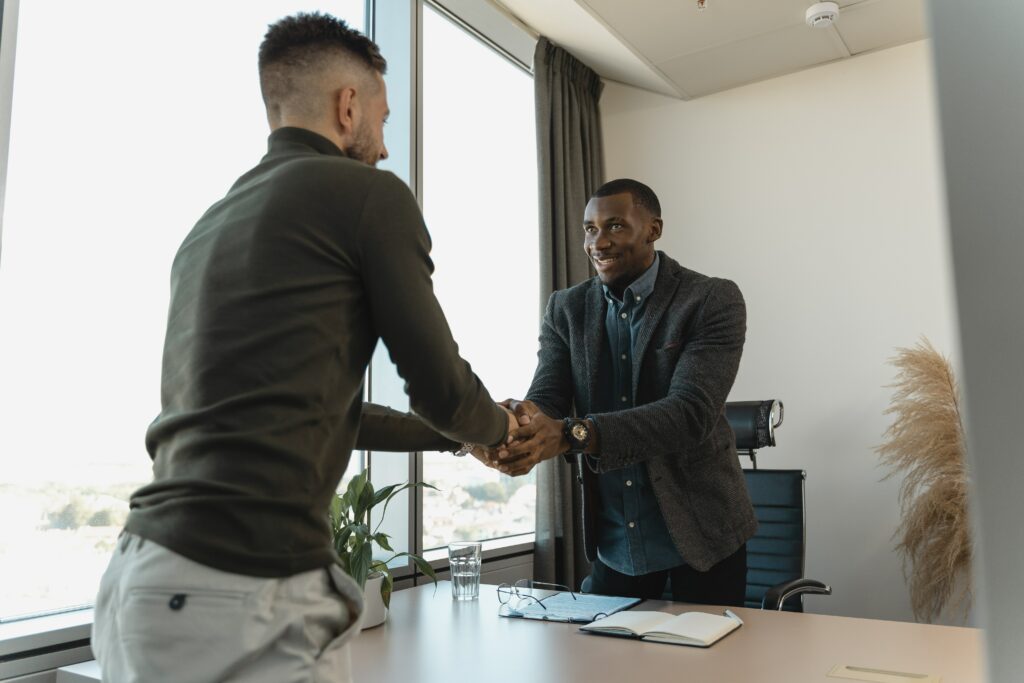 Two men standing at a desk, shaking hands and smiling.